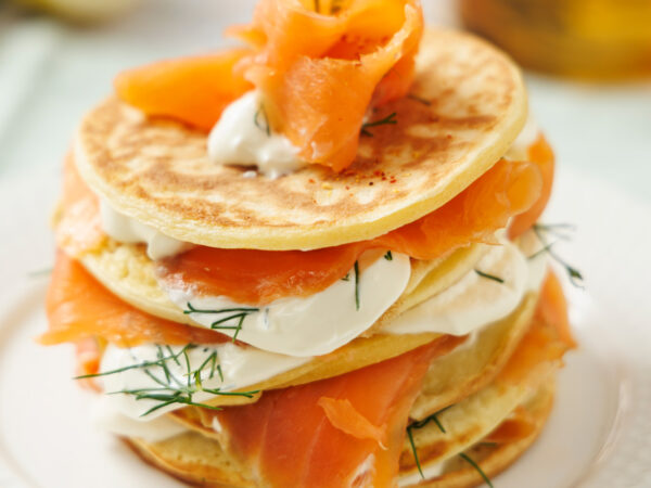 Millefeuille de blinis avec des tranches de truite fumée et crème fouettée à l'aneth et au citron, dressé dans une assiette blanche